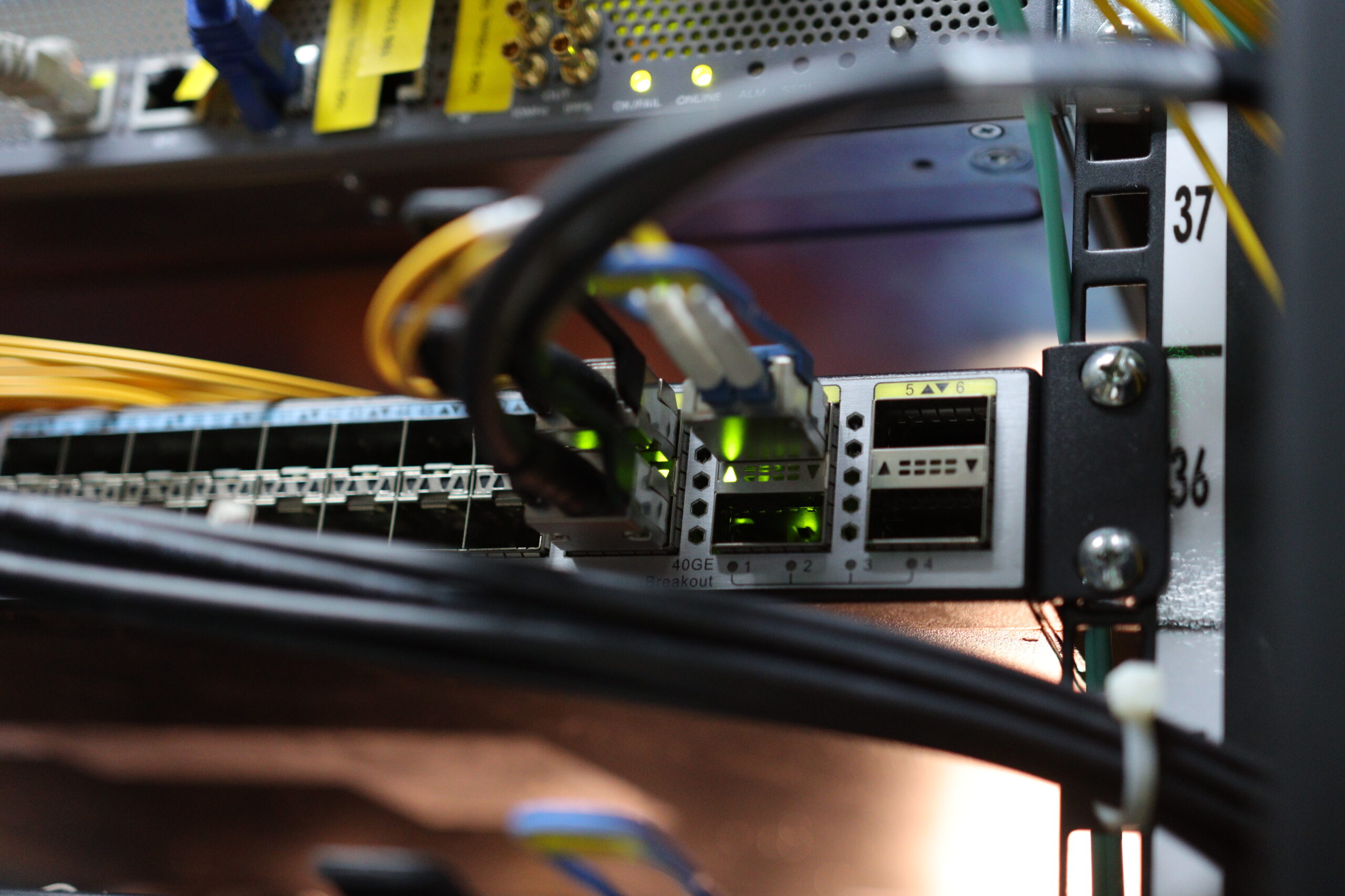 Network switch in a server rack with connected fiber optic cables and active green LED link lights